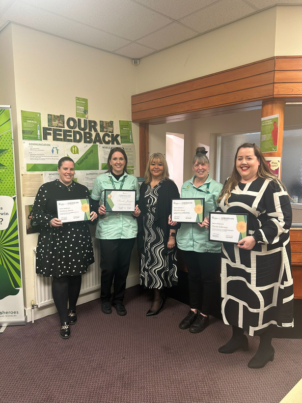 five hales care workers holding certificates in front of a wall